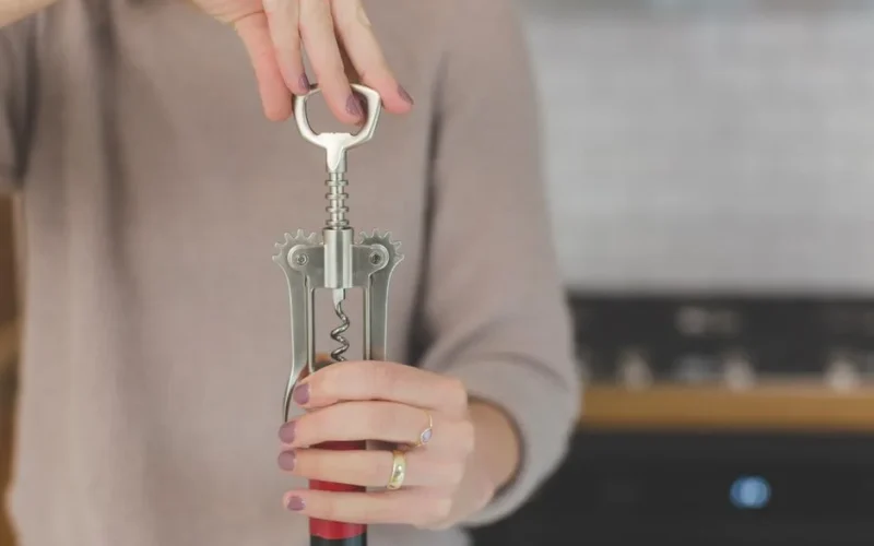 Close-up of a woman using a corkscrew to open a wine bottle indoors.