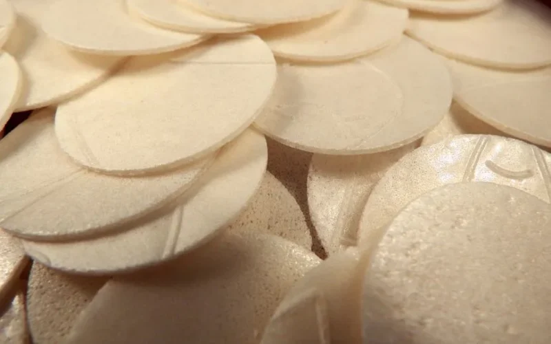 High angle closeup of many thin white Communion bread hosts used in Christian ritual of Eucharist
