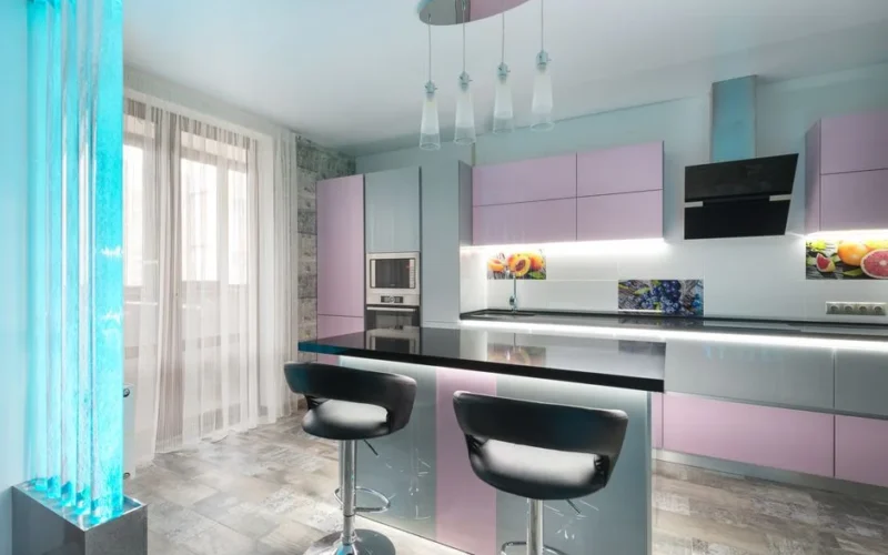 Interior of modern kitchen with chairs at counter placed near colorful cupboards with contemporary appliances in spacious room with bubble wall and window