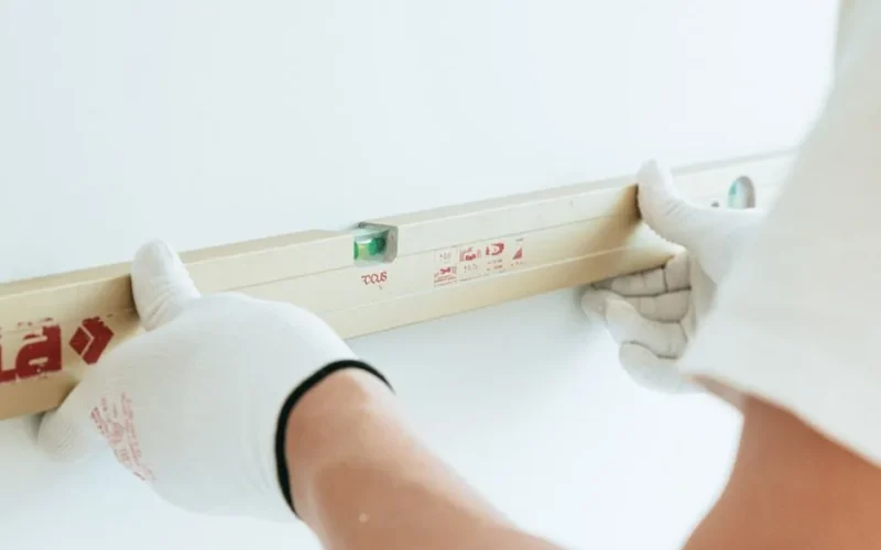 Hands in white gloves using spirit level on wall for precise leveling.