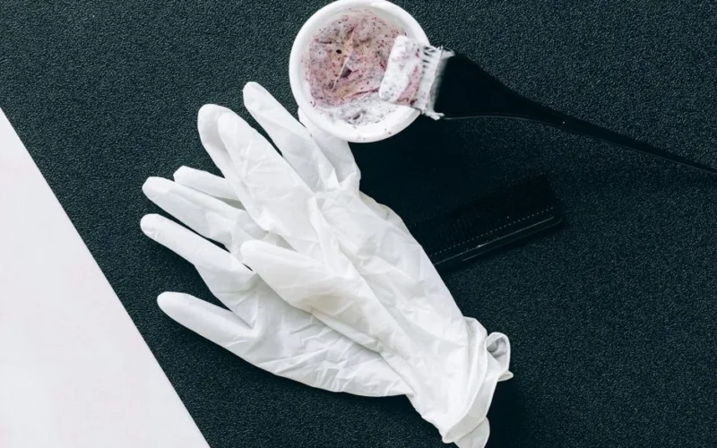 Flat lay of hairdressing tools including dye brush, latex gloves, hair dye bowl, and comb.