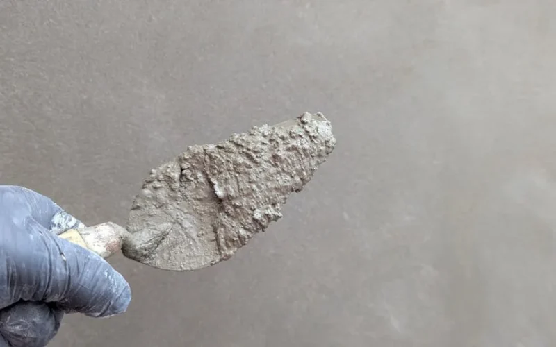 Hand wearing glove holds plaster trowel against smooth wall, depicting construction work.