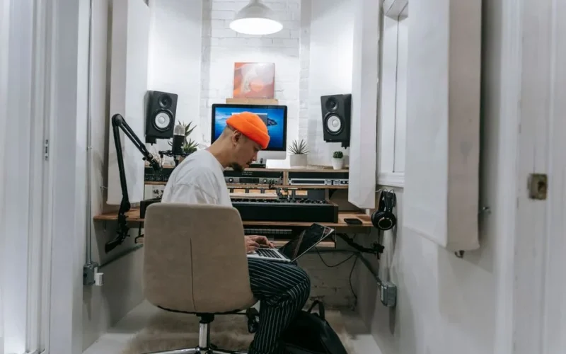 An adult male focuses on music production in a sleek, white recording studio setting.