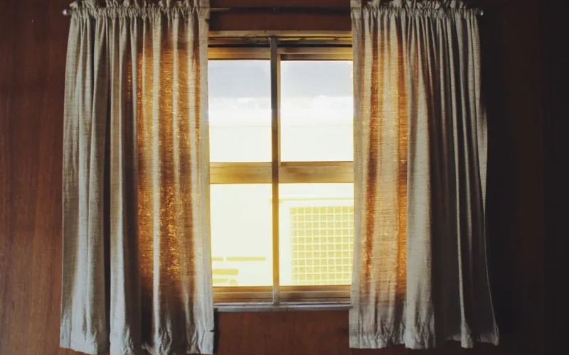 Warm sunlight streaming through fabric curtains in a wooden interior setting.