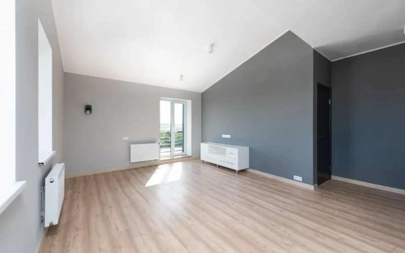Wide-angle shot of a modern unfurnished apartment with wooden flooring and large windows.