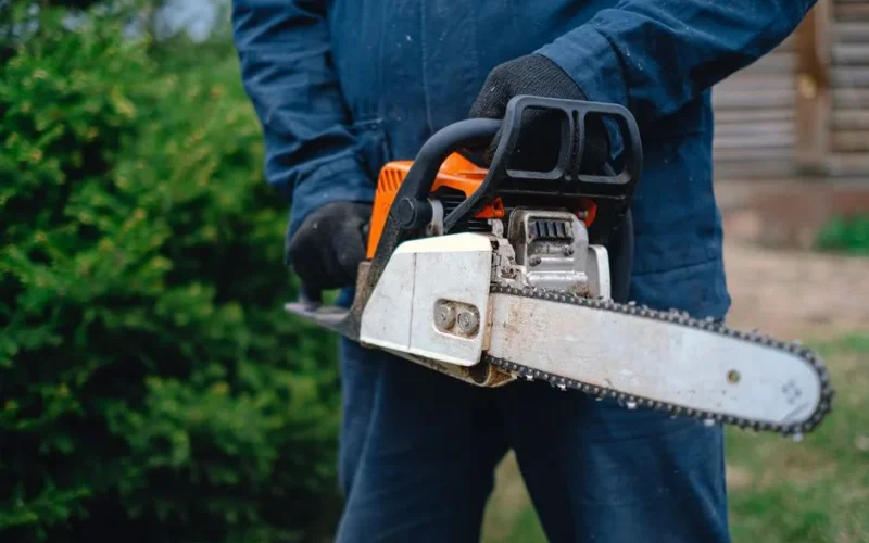 Close-up of a worker holding a chainsaw, ideal for carpentry and outdoor renovations, captured outdoors.