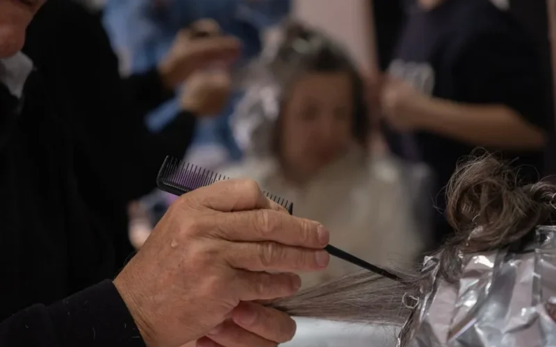 Hair salon scene with a hairdresser using foil and comb for highlights.
