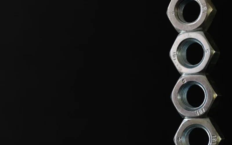 Detailed photo of four stacked hex nuts against a black background highlighting industrial design.
