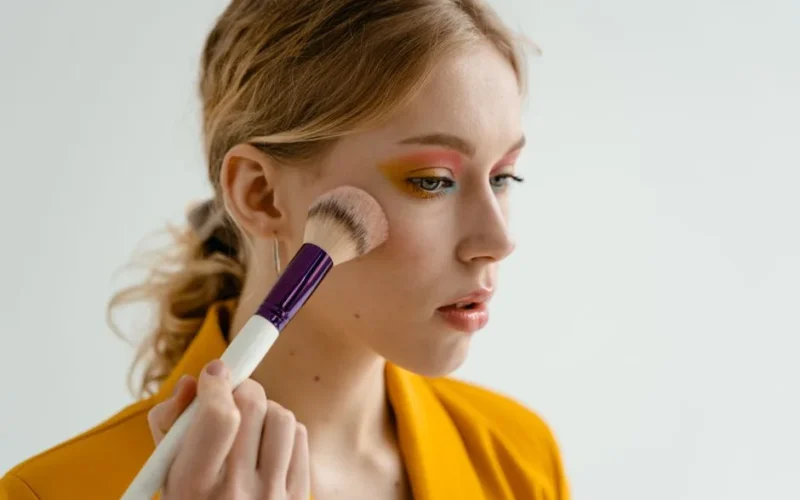 Woman using a makeup brush to apply blush, showcasing beauty and cosmetics indoors.
