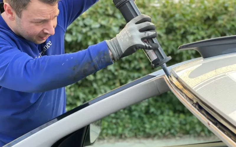 Man carefully applies glue to repair car windshield in Copenhagen outdoor setting.