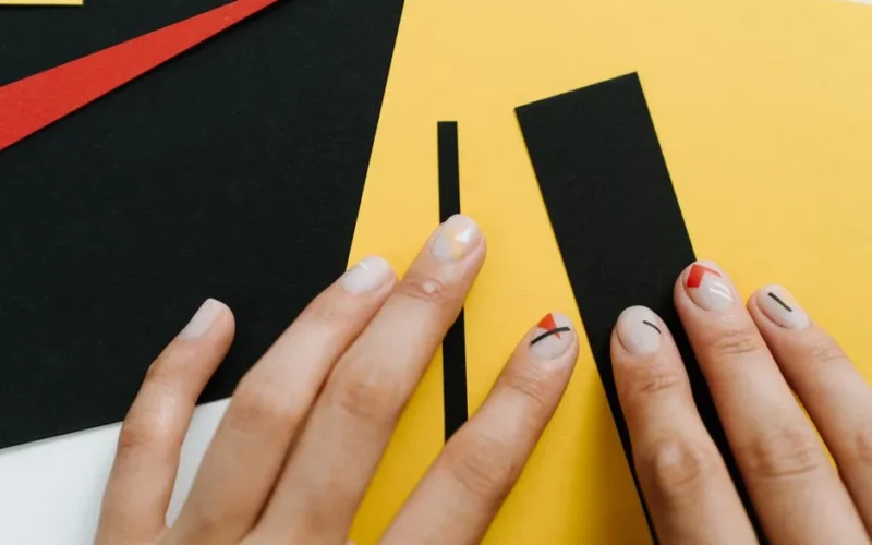Close-up of modern nail art with geometric shapes on a yellow and black paper collage.