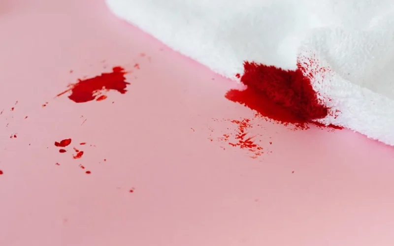A white towel with red stains on a pink surface, depicting a messy spill.