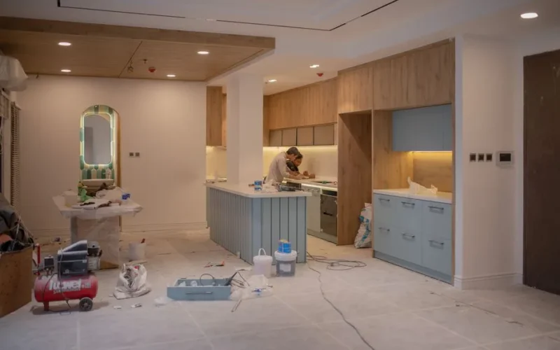 A modern kitchen undergoing renovation, featuring a worker, tools, and materials.