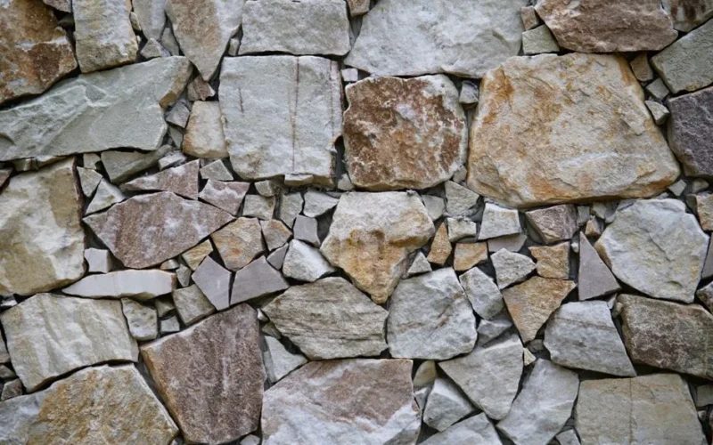Close-up of a natural stone wall with irregular patterns of beige and gray rocks in various sizes.