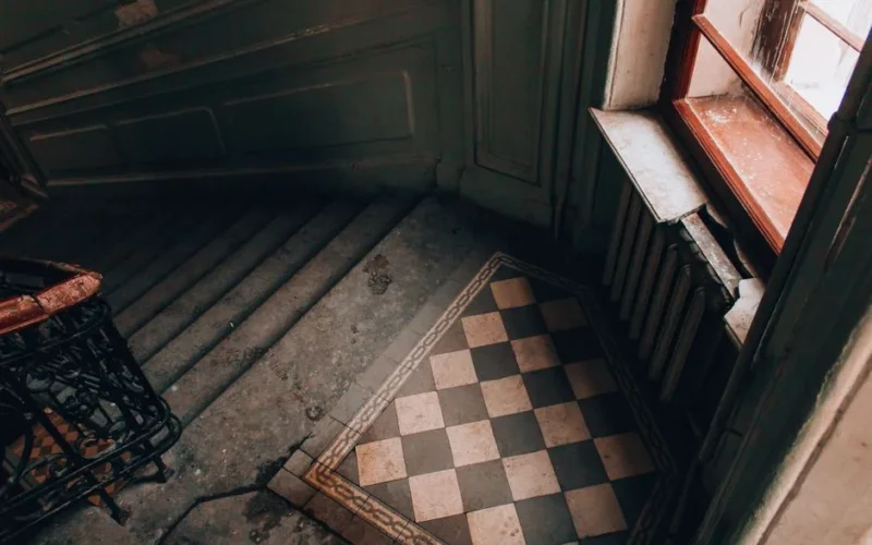 An old stairway featuring a vintage look with checkered tiles and ornate railing.