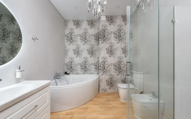 Bath against bidet and mirror above washstand in contemporary bathroom with chandelier and ornamental wall in house