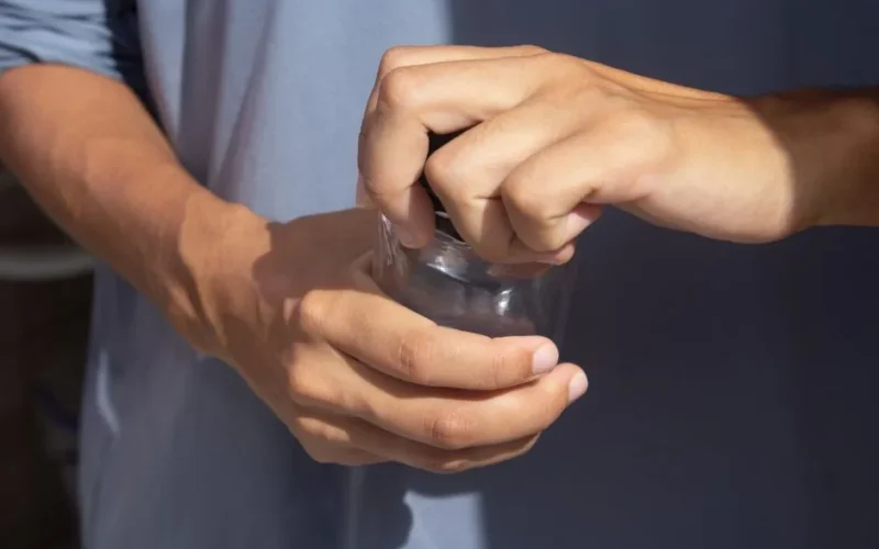 Close-up view of hands opening a jar outdoors, emphasizing grip and strength.